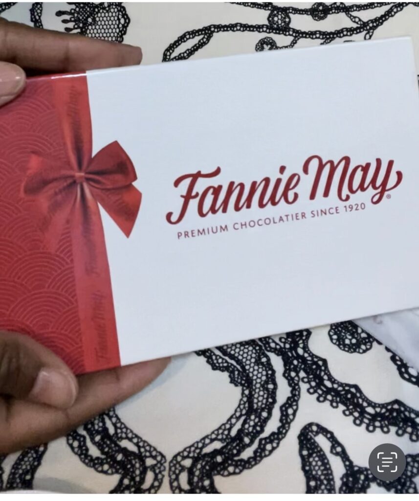 A rectangular box of Fannie May chocolates wrapped in a red bow.